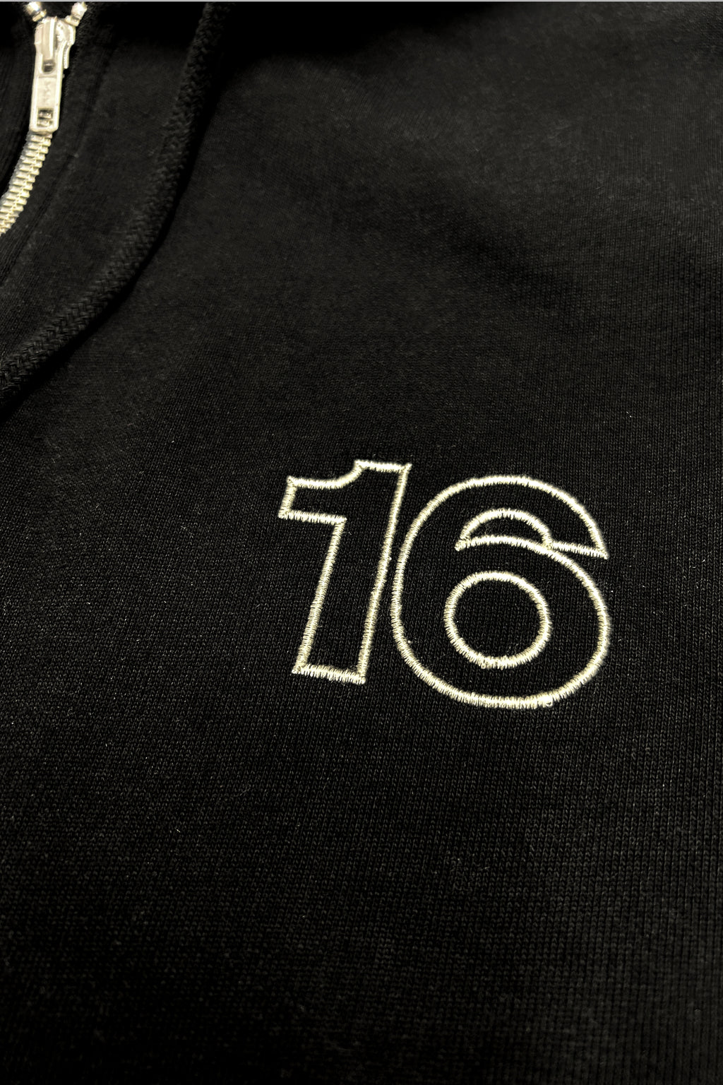Close-up of 16 Sixteen embroidered logo on TRIBE WEAR zip-up hoodie