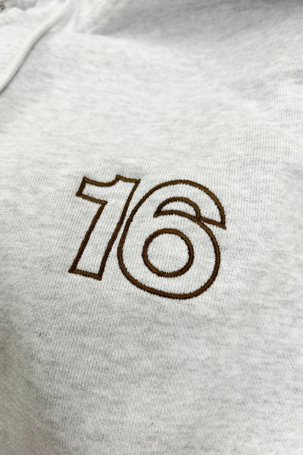 Close-up of 16 Sixteen embroidered logo on TRIBE WEAR zip-up hoodie