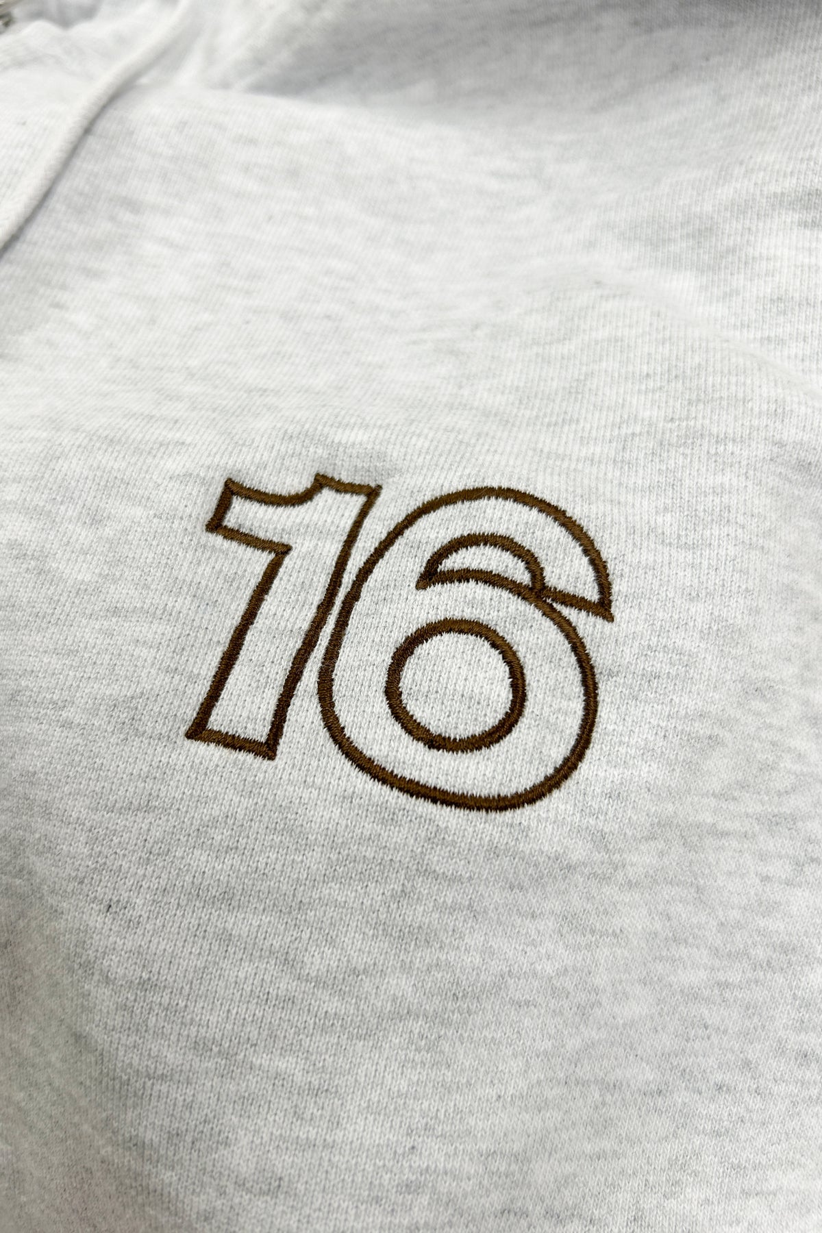 Close-up of 16 Sixteen embroidered logo on TRIBE WEAR zip-up hoodie